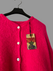 Pink cardigan on a hanger with a colorful tag against a plain background