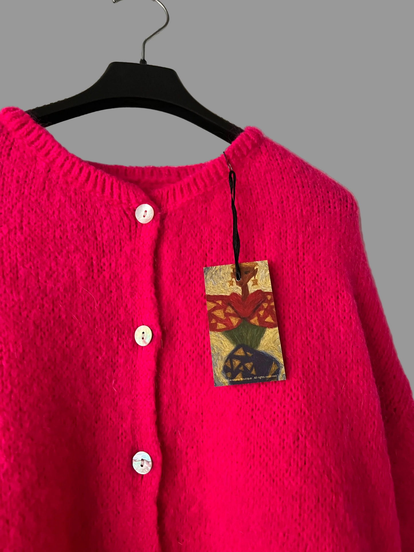 Pink cardigan on a hanger with a colorful tag against a plain background