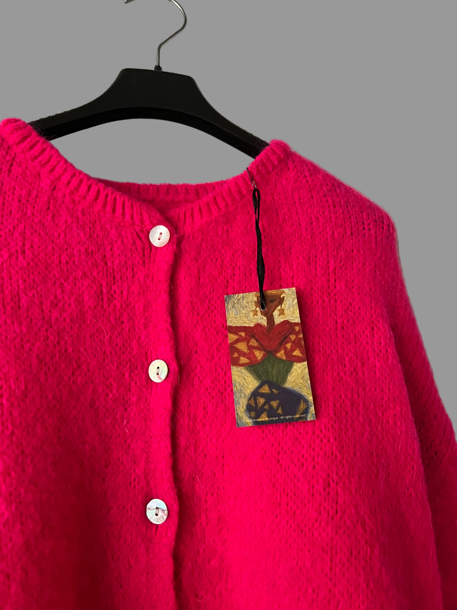 Pink cardigan on a hanger with a colorful tag against a plain background